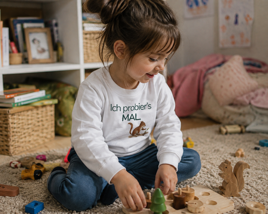 Mädchen sitzt auf dem Fußboden mit einem Kinder Sweatshirt mit Eichhörchen und dem Spruch Ich probier's mal und spielt.