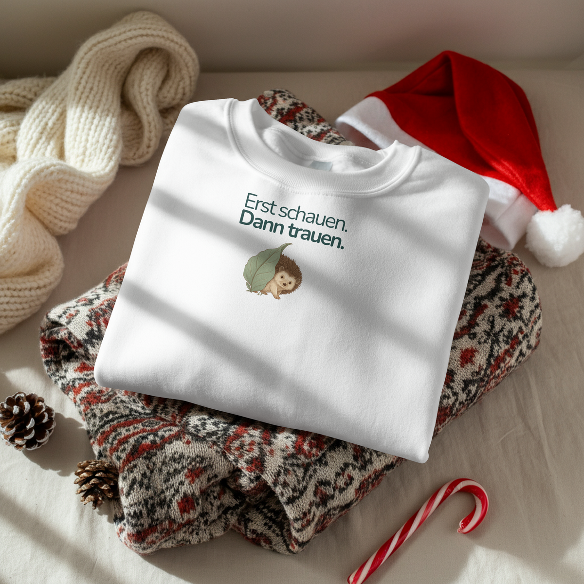 Sweatshirt als Weihnachtsgeschenk mit der Botschaft Igel "Erst schauen - dann trauen". Weihnachtliche Umgebung mit einer Nikolausmütze.