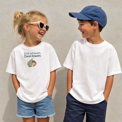 Ein Junge und ein Mädchen stehen nebeneinander an einer Wand und schauen sich an. Das Mädchen trägt ein weißes Kinder-Tshirt mit einem Igel und der Aufschrift Erst schauen. Dann trauen. Der Junge trägt ein weißes Kinder T-Shirt ohne Aufschrift.