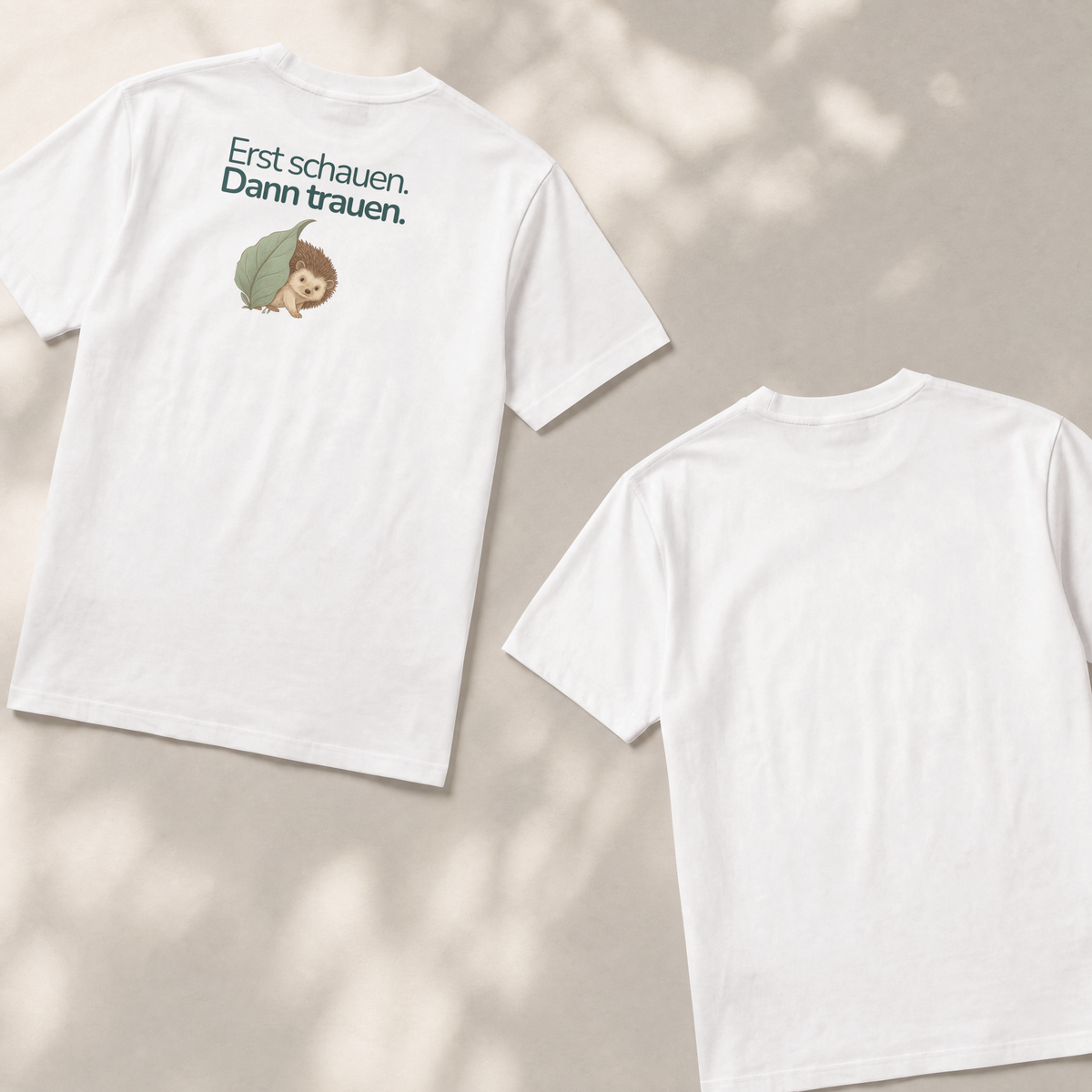 Zwei Kinder T-shirts liegen flach auf dem Boden. Die Vorderseite zeigt einen Igel mit dem Spruch Erst schauen. Dann trauen. Die Rückseite ist weiß und nicht bedruckt.