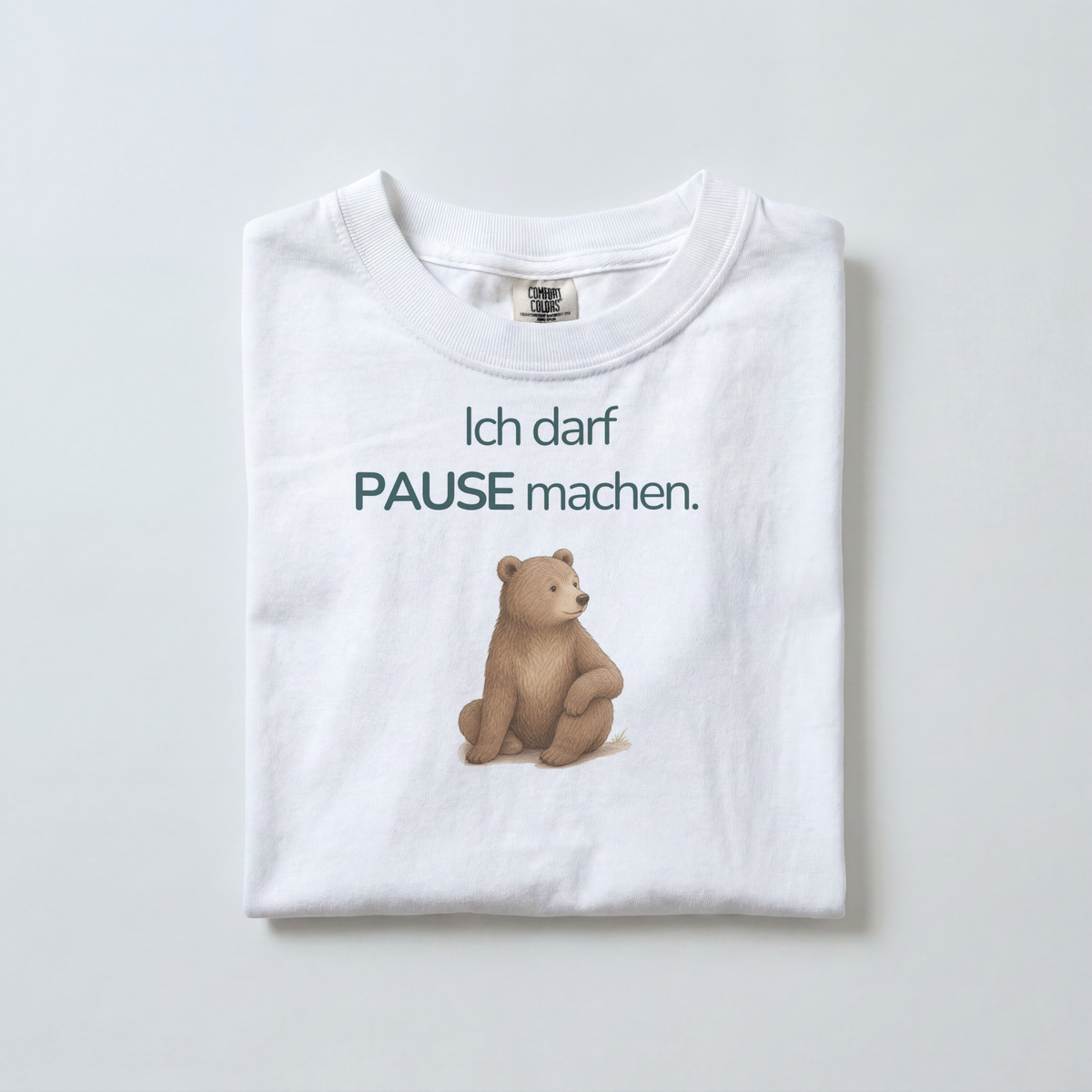 Ein weißes gefaltetes Kinder T-Shirt liegt auf dem Boden. Es zeigt einen Bär mit dem Spruch Ich darf Pause machen