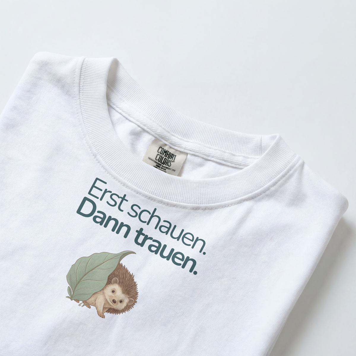 Gezeigt wird der Halsauschnitt eines weißes Kinder T-Shirts mit einem Igel und dem Spruch Erst schauen. Dann trauen.