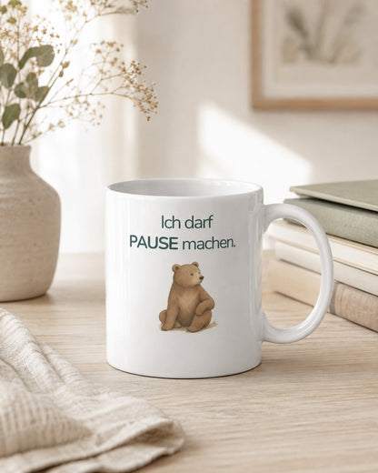 Eine Kindertasse mit einem Bären und dem Spruch Ich darf Pause machen steht auf einem Tisch.