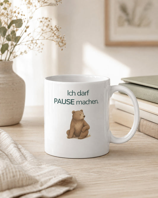 Eine Kindertasse mit einem Bären und dem Spruch Ich darf Pause machen steht auf einem Tisch.