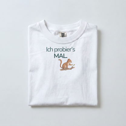 Ein weißes gefaltetes Kinder T-Shirt liegt auf dem Boden. Es zeigt ein Eichhörnchen mit dem Spruch Ich probier's mal