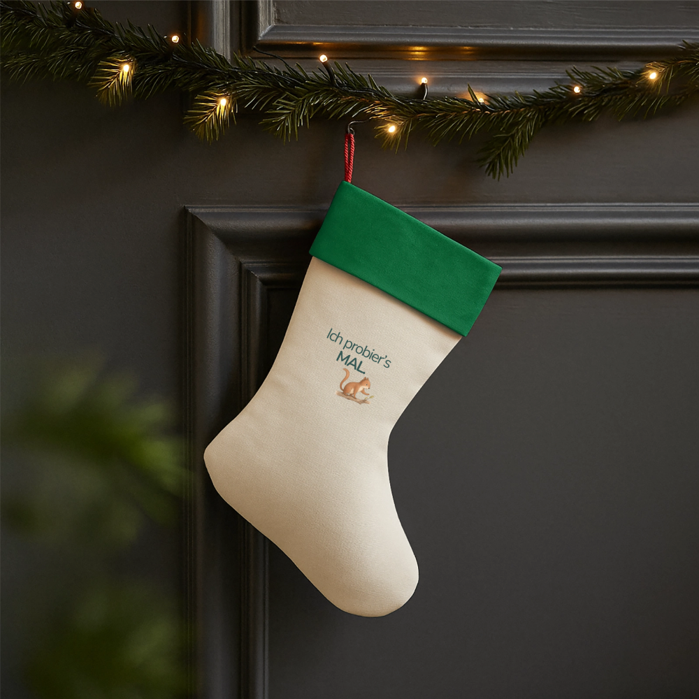 Ein Weihnachsstrumpf mit grünem Saum und der Botschaft "Ich probiers mal" und dem Motiv Eichhörnchen hängend an einer Tür.