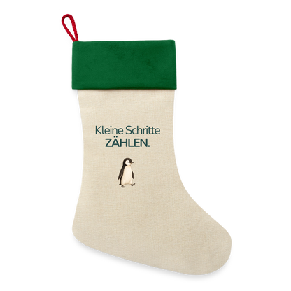 Ein Weihnachsstrumpf mit grünen Saum und der Botschaft "Kleine Schritte Zählen." und dem Motiv Pinguin.