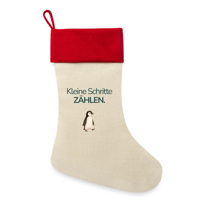 Ein Weihnachsstrumpf mit rotem Saum und der Botschaft "Kleine Schritte Zählen." und dem Motiv Pinguin.