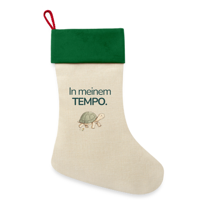 Ein Weihnachsstrumpf mit grünen Saum und der Botschaft "In meinem Tempo." und dem Motiv Schildkröte.