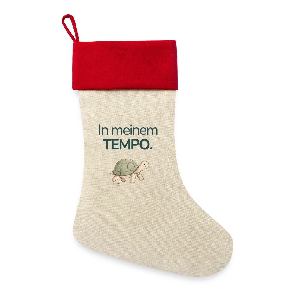 Ein Weihnachsstrumpf mit rotem Saum und der Botschaft "In meinem Tempo." und dem Motiv Schildkröte.