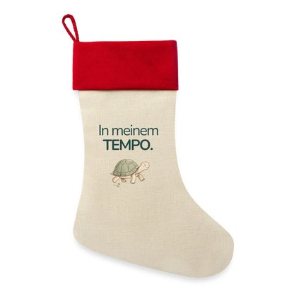 Ein Weihnachsstrumpf mit rotem Saum und der Botschaft "In meinem Tempo." und dem Motiv Schildkröte.