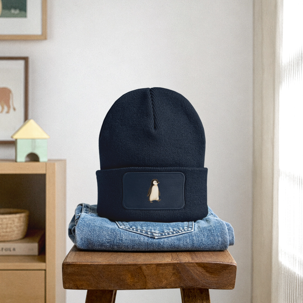 Kinder Beanie mit dem Pinguin in dunkelblau, steht auf einer gefalteten Jeans