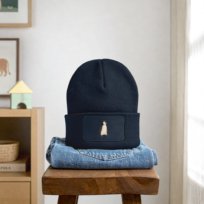 Kinder Beanie mit dem Pinguin in dunkelblau, steht auf einer gefalteten Jeans