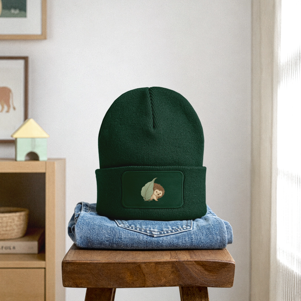 Kinder Beanie mit dem Igel in dunkelgrün, steht auf einer gefalteten Jeans