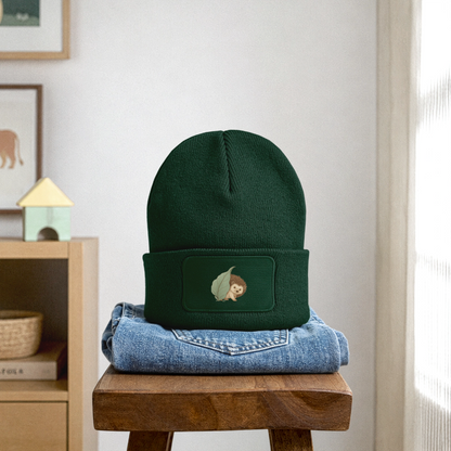 Kinder Beanie mit dem Igel in dunkelgrün, steht auf einer gefalteten Jeans